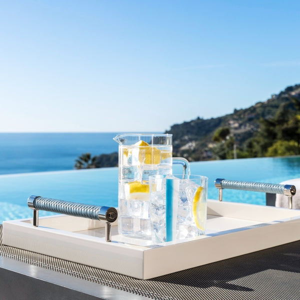 Clear pitcher of lemon water on a tray with a scenic background of ocean and mountains.