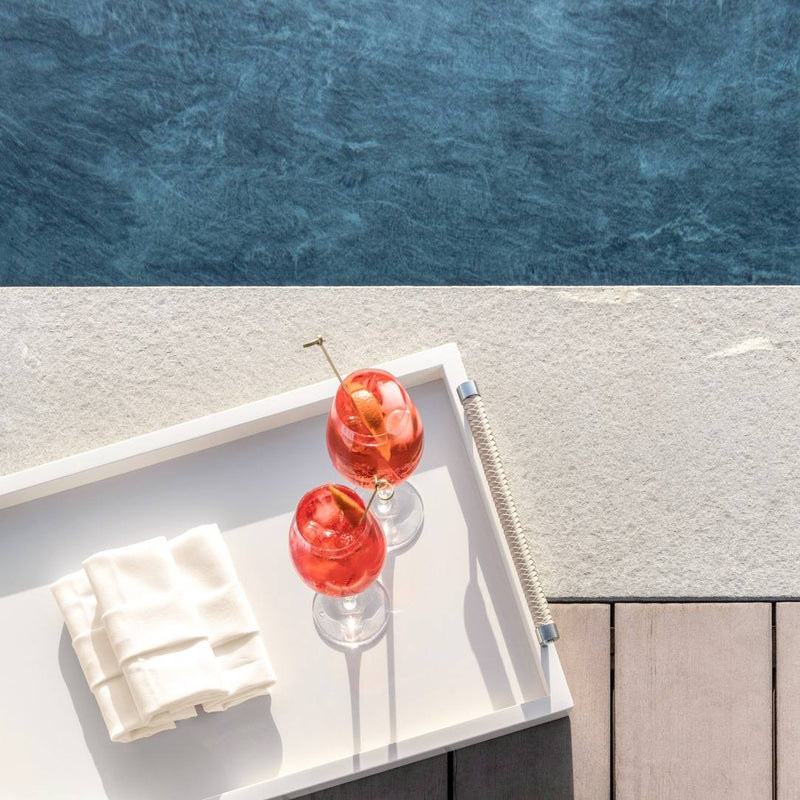 Two red cocktails with a cherry on a white tray by a pool.