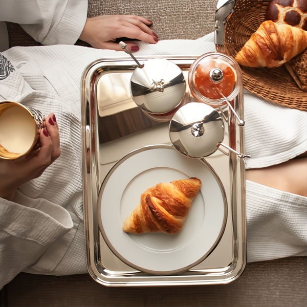 London tray silver-plated by Sonja Quandt with a croissant and small dishes, person holding a cup, sitting on a textured surface.