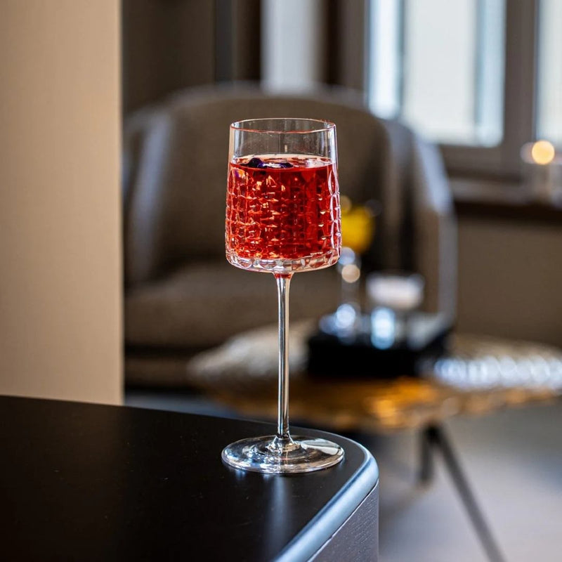 Glass of red wine with berries on a table in a cozy room.