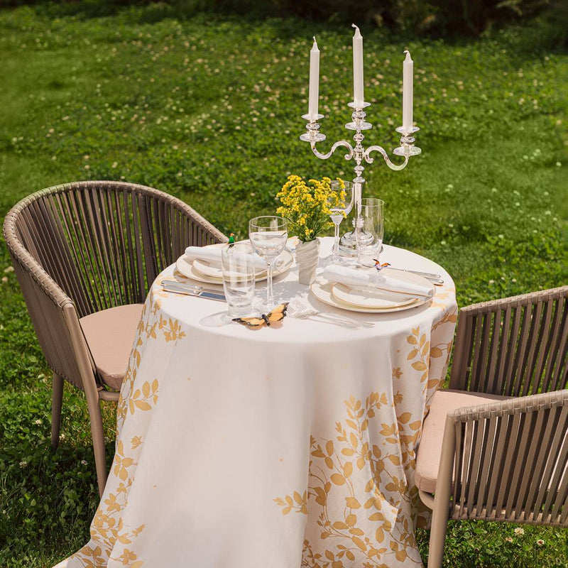 Dining table set with a floral tablecloth, Regina candle from Edzard, and glasses outdoors on grass.