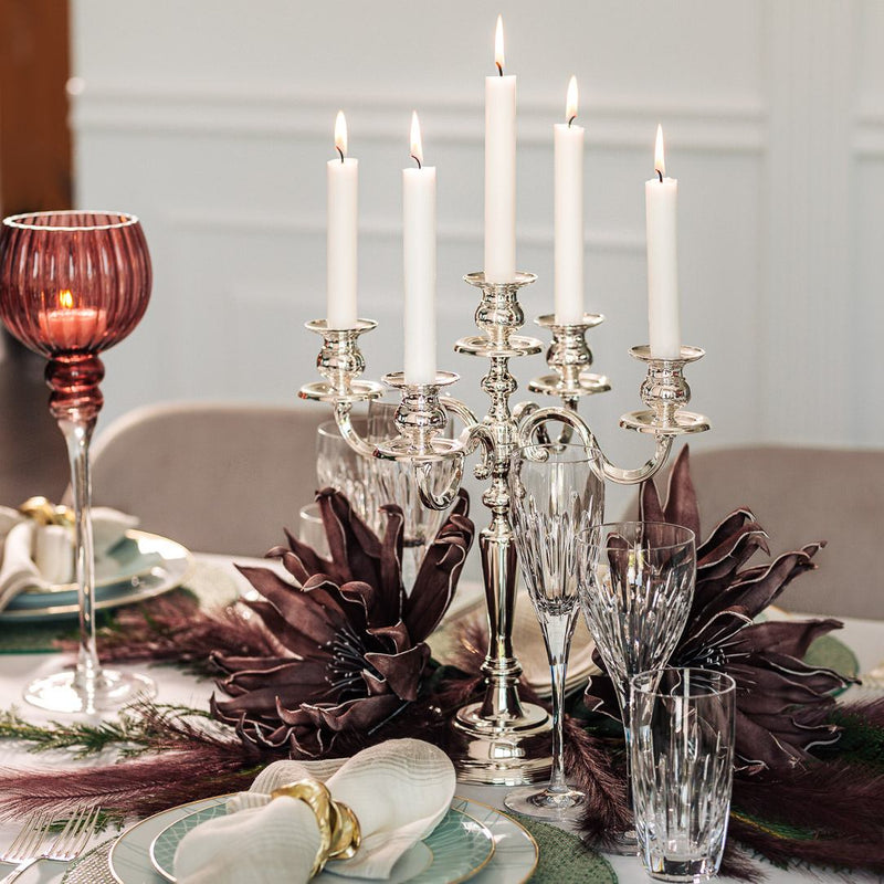 Silver candelabra with lit candles on a table setting with purple napkins and glasses.