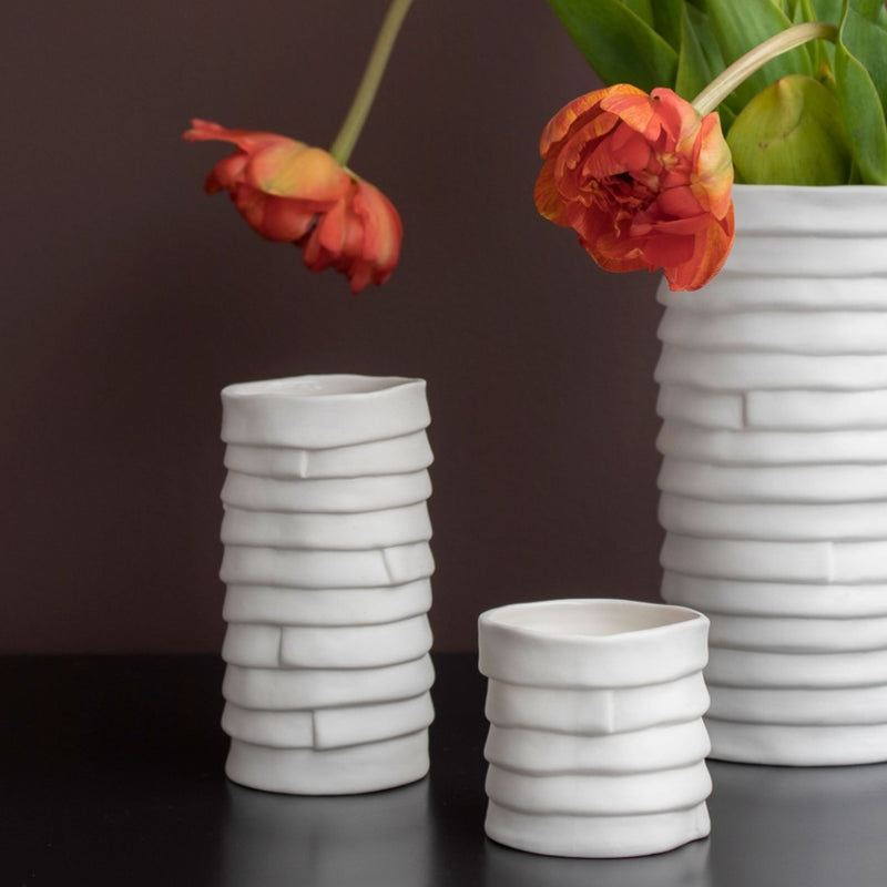 Three white ceramic vases with textured designs on a dark surface.