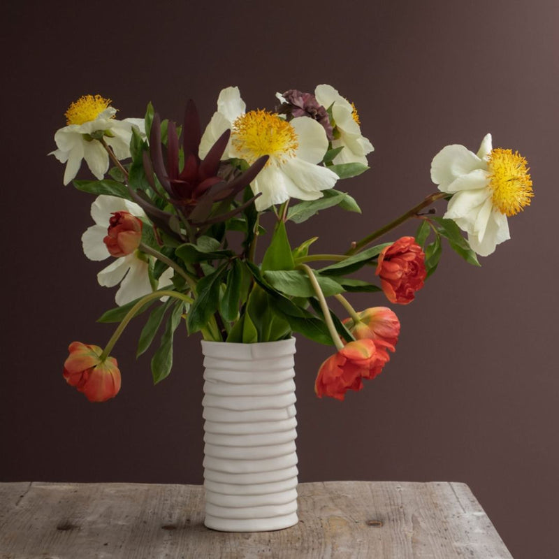 Bouquet of flowers in a white vase on a wooden surface with a dark background