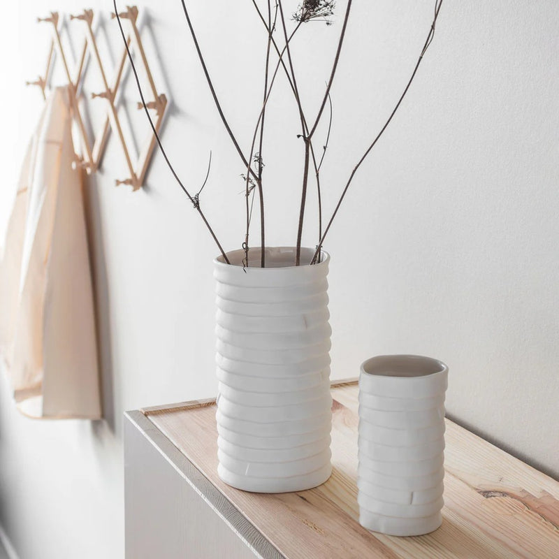 Two white textured vases on a wooden surface with a minimal background