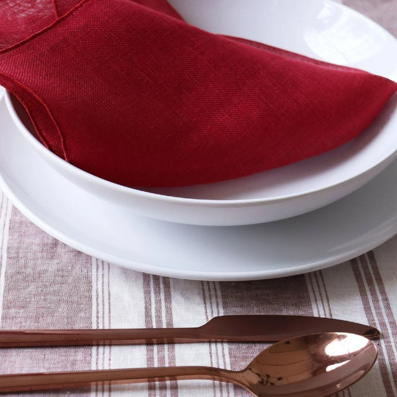 Copper spoon on a striped tablecloth with a red napkin and white plates.