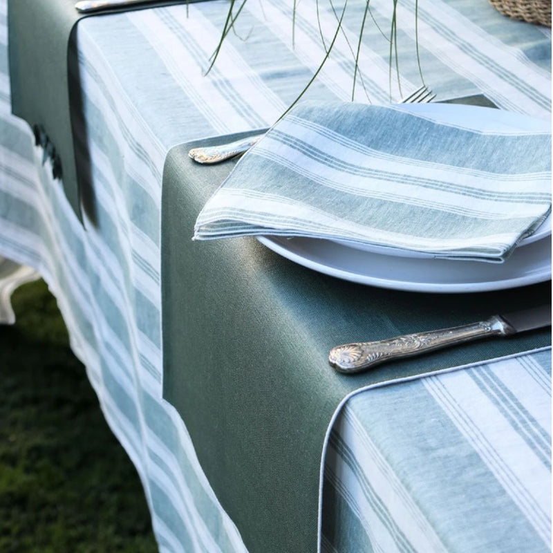 Table setting with striped tablecloth, plates, and silverware on a green surface.