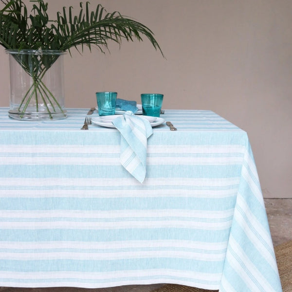 Table setting with a striped tablecloth, blue glasses, and a plant on a neutral background