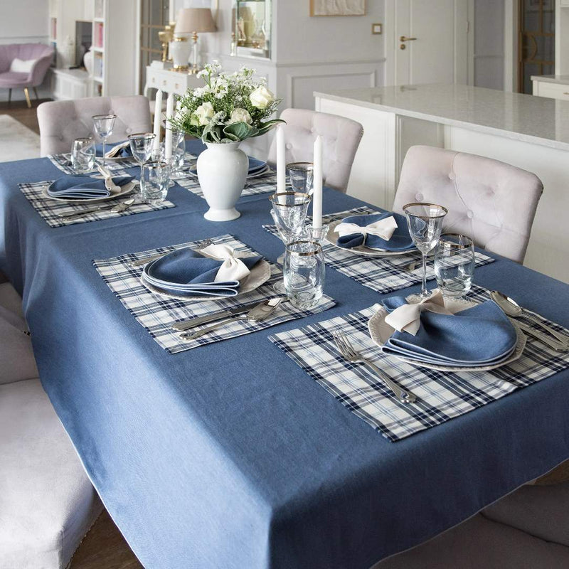 Dining table set with blue tablecloth, plaid placemats, and white floral centerpiece.