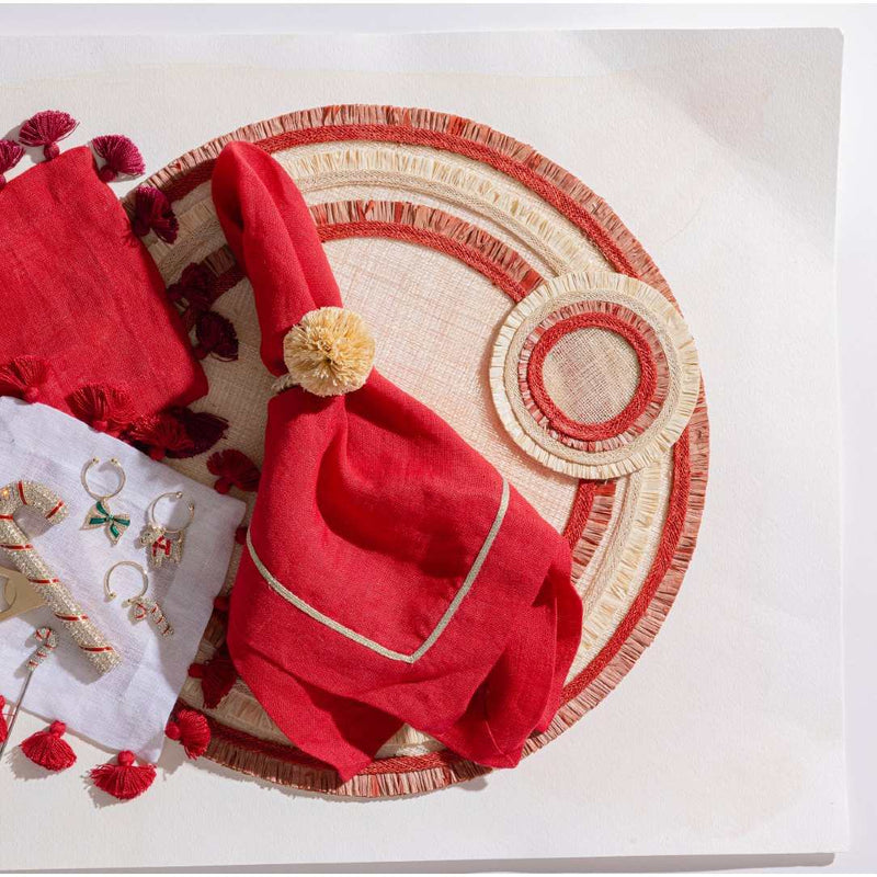 Red napkin with pom-pom on a decorative placemat and coaster with jewelry and red flowers on a white surface
