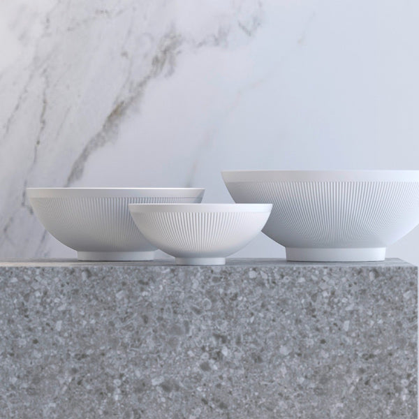 Three white ceramic bowls on a gray surface with a marble wall background
