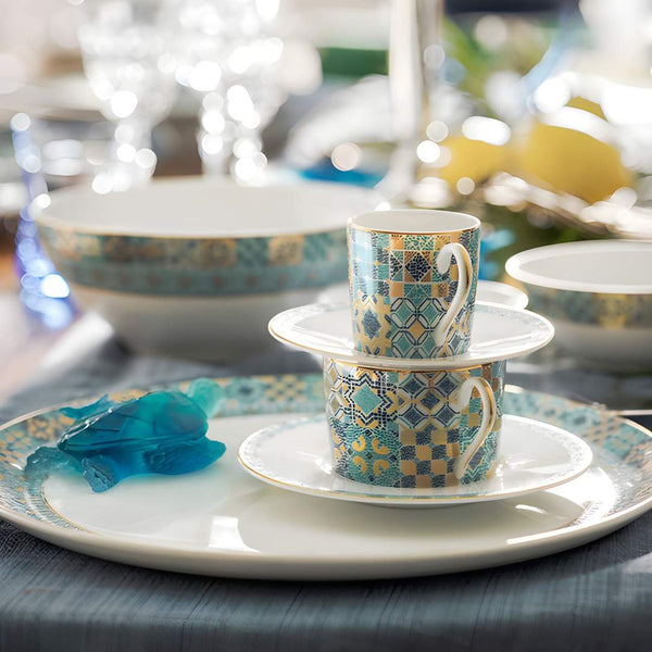 Two patterned teacups stacked on saucers with a blurred background of a dining setting.