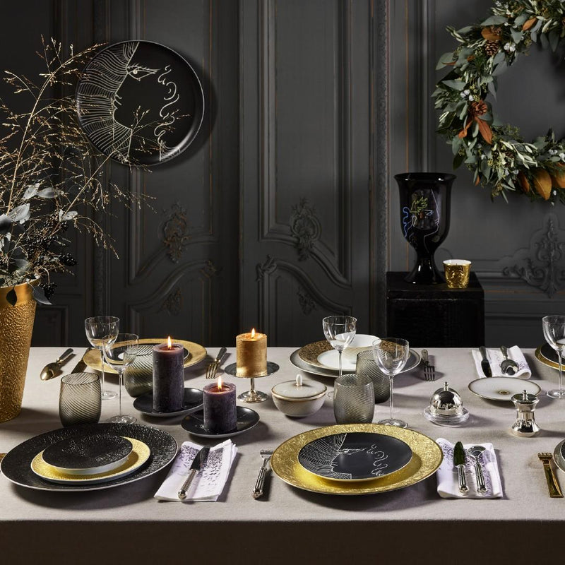 Elegant dining table setting with gold and black plates, candles, Salt and Pepper Mill Regards Silver-Plated by Ercuis and decorative items against a dark wall.