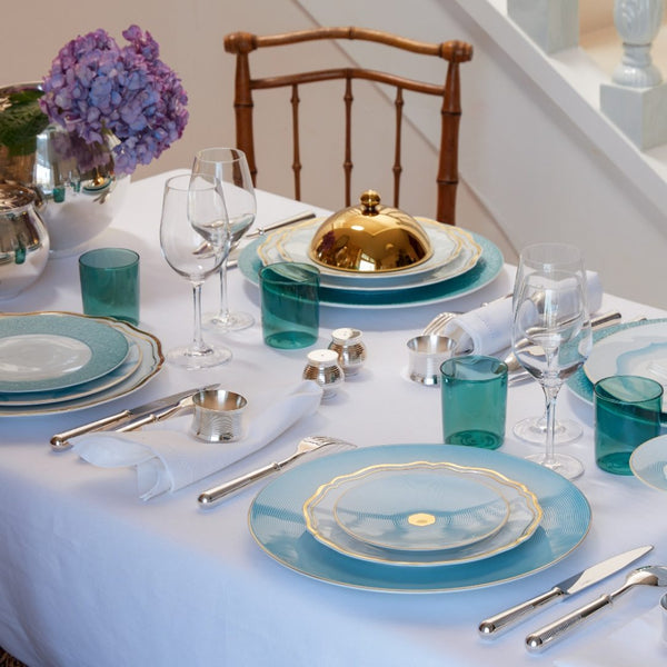 Elegant table setting with blue and gold plates, glasses, and Salt and Pepper Shakers Transat Silver-Plated by Ercuis, on a white tablecloth.