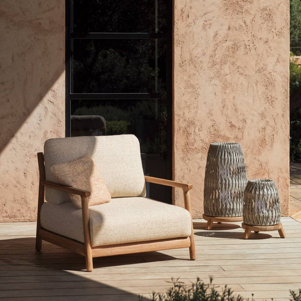 Beige armchair on a wooden deck with textured walls and Sandua lanterns by Manutti