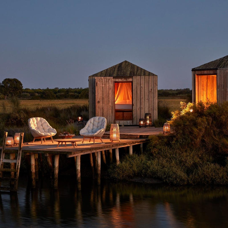 Wooden cabin by a body of water with outdoor seating area at dusk.