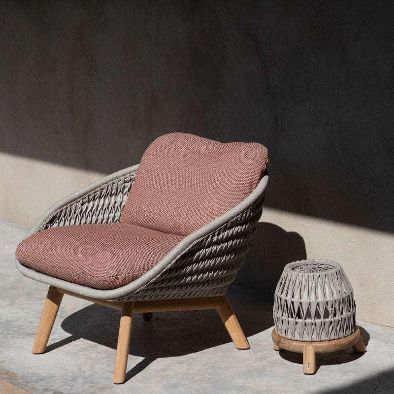 Woven chair with pink cushion and small matching table on a concrete surface.