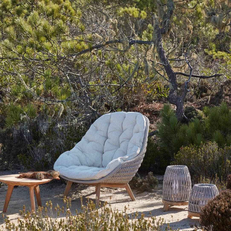 Wicker chair with quilted cushion and Sandua lantern by Manutti in a natural outdoor setting