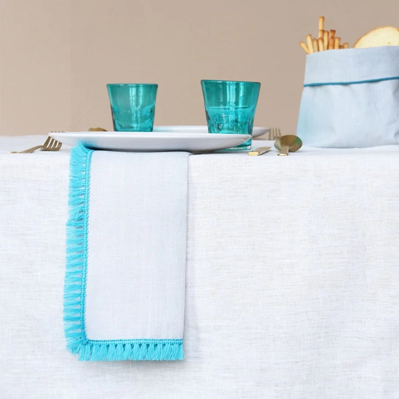 Table setting with white tablecloth, blue napkin, and turquoise glasses.