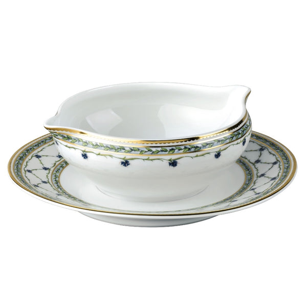 A white porcelain sauce boat with blue floral patterns and gold accents, accompanied by a round stand with a matching design.