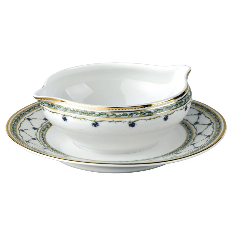 A white porcelain sauce boat with blue floral patterns and gold accents, accompanied by a round stand with a matching design.