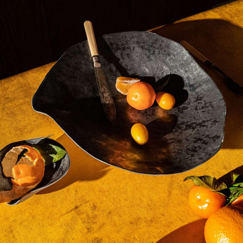 Oranges on a Modern graphite porcelain large dinner plates No6 Indulge by Sarah-Linda with a knife, on a yellow textured background