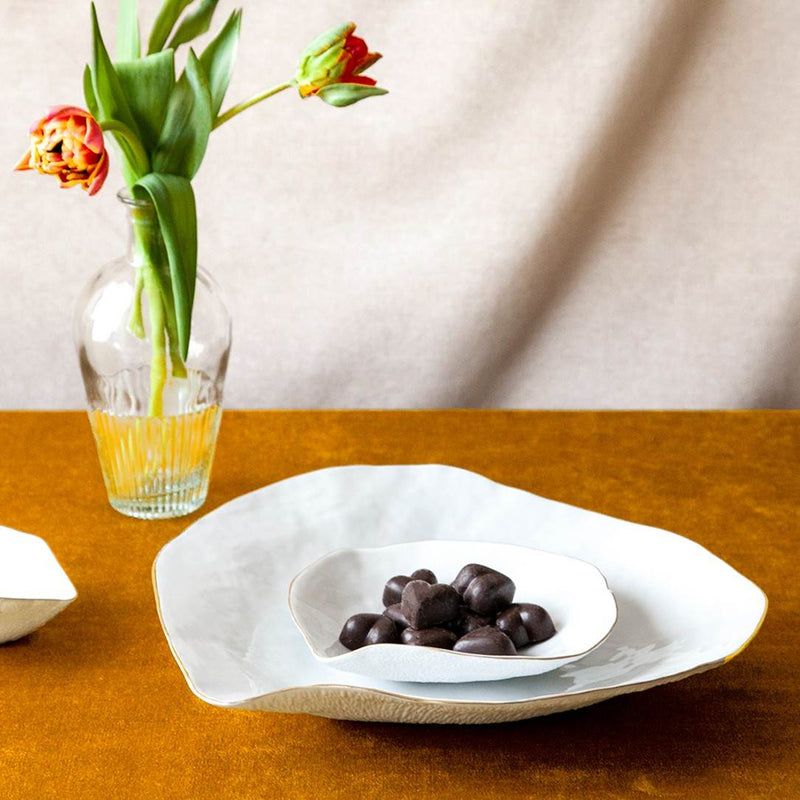Shell-inspired porcelain large dinner plates White with Golden Rim No6 Indulge with chocolate truffles on a wooden table, next to a vase with flowers.