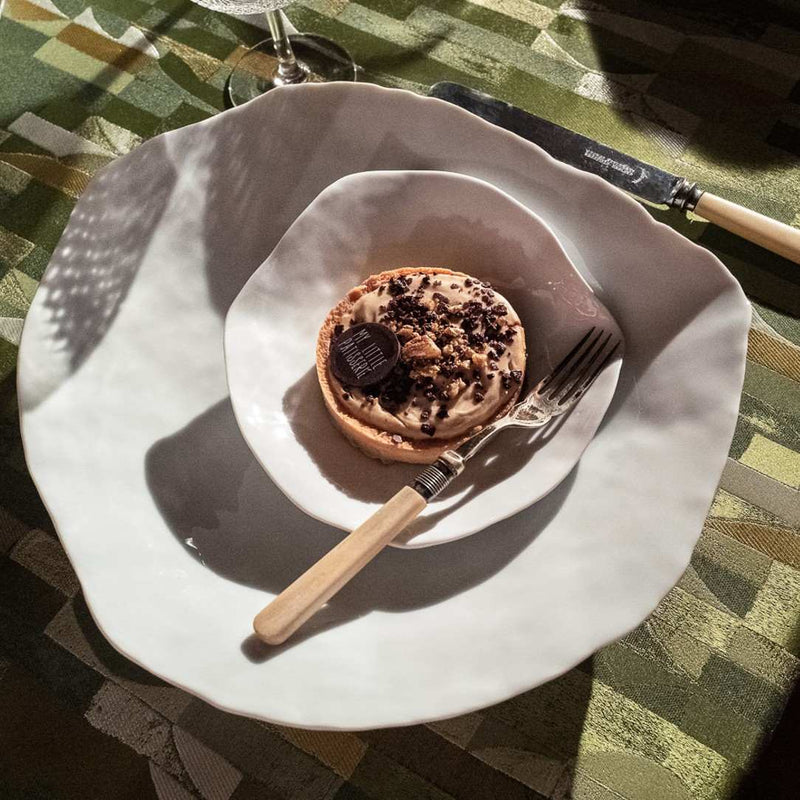 Small dessert on a luxury Limoges porcelain large dinner plate White No6 Indulge Sarah-Linda with a fork and knife on a checkered tablecloth