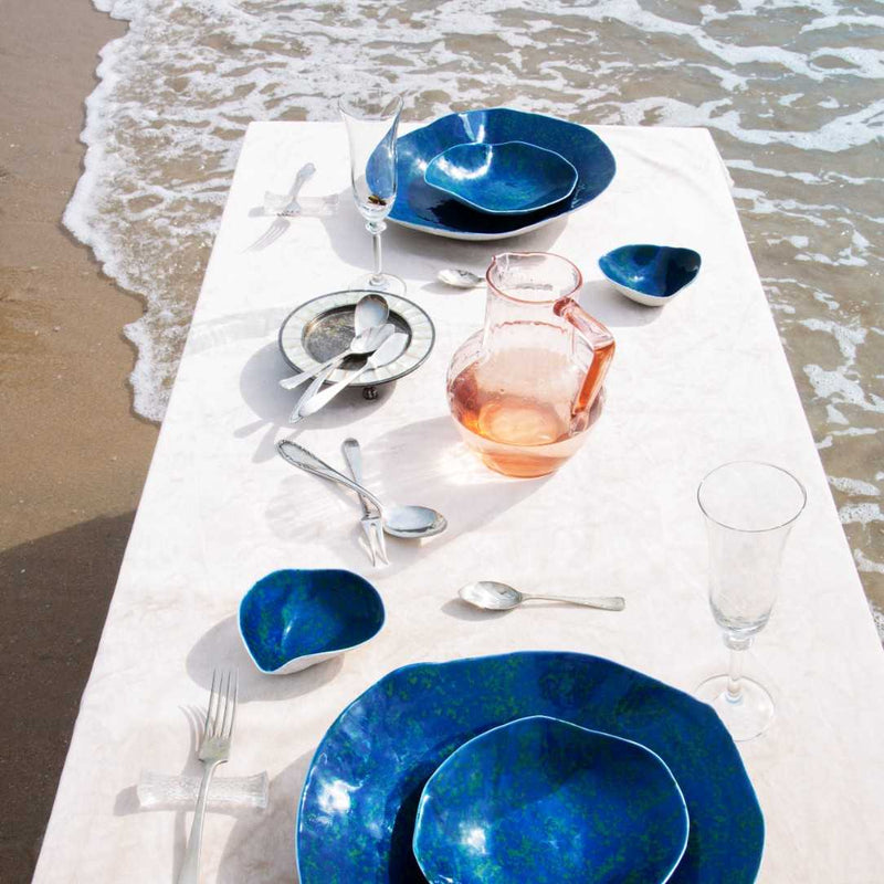 Dinner setup on a tablecloth with Shell-inspired porcelain side bowls blue-green interior No2 Indulge Sarah-Linda and glasses by the beach.