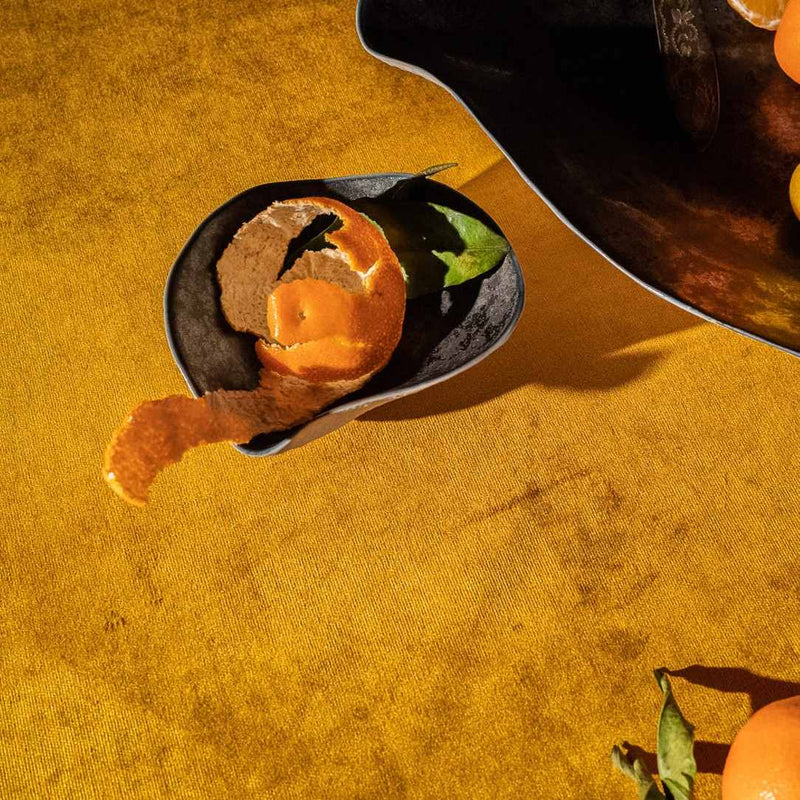 Close-up of Sculptural porcelain side bowls dark graphite No2 Indulge Sarah-Linda an orange slice on a yellow surface