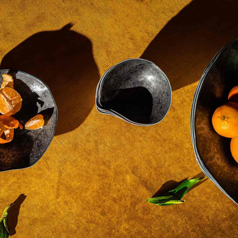Sculptural porcelain side bowls dark graphite No2 Indulge Sarah-Linda on a textured orange surface with fruits inside.