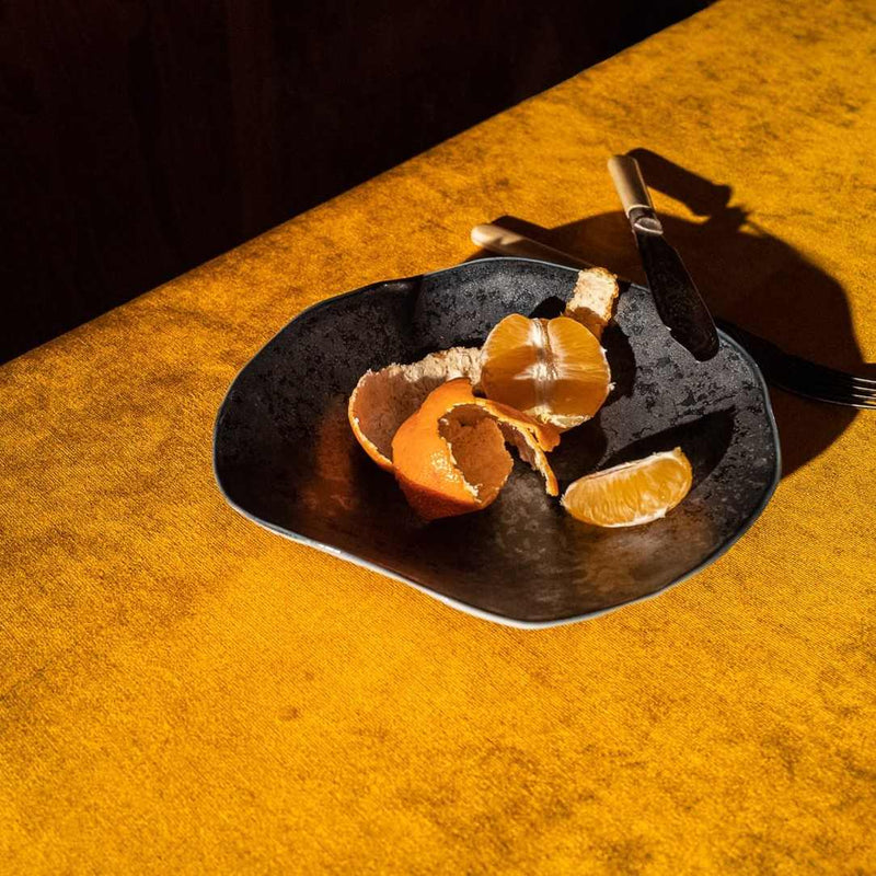 Orange peels on a Sculptural porcelain small plates Graphite No5 Indulge Sarah-Linda with a knife on a yellow surface