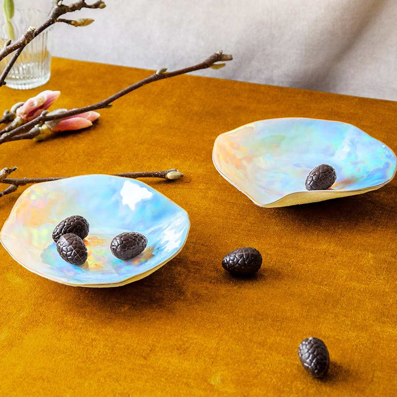 Two iridescent shell-shaped dishes on a wooden surface with decorative branches and flowers.
