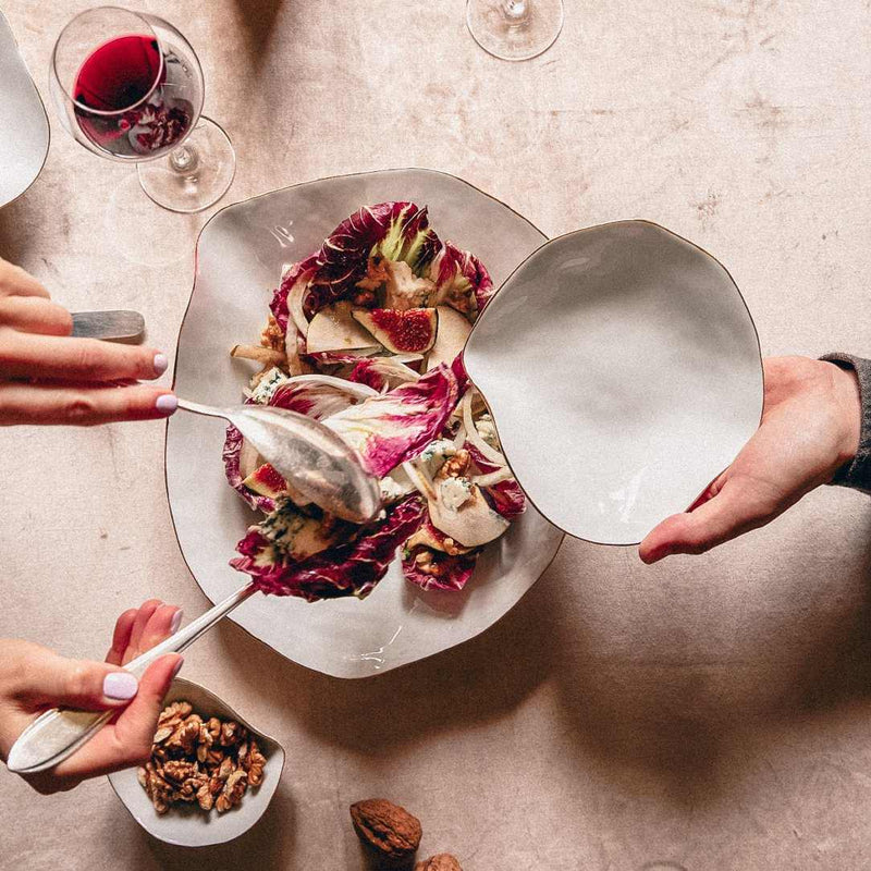 Shell-inspired porcelain small plates White with gold rim No5 Indulge collection with a side of nuts on a beige table.