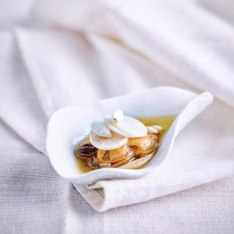 Shell-inspired porcelain white spoons Nº1 Indulge Sarah-Linda with food on a white cloth