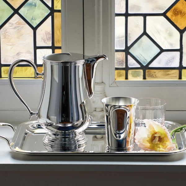 Luxury silver-plated water jug Rencontre by Ercuis – with a stained glass window in the background