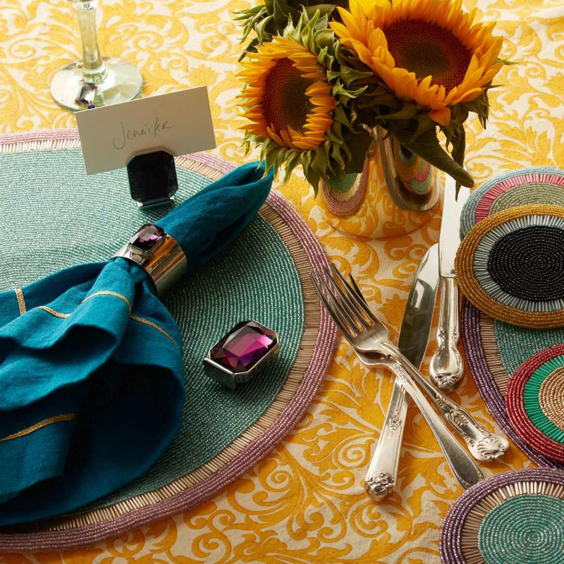 Decorative table setting with sunflowers, colorful plates, and silverware on a yellow patterned tablecloth.
