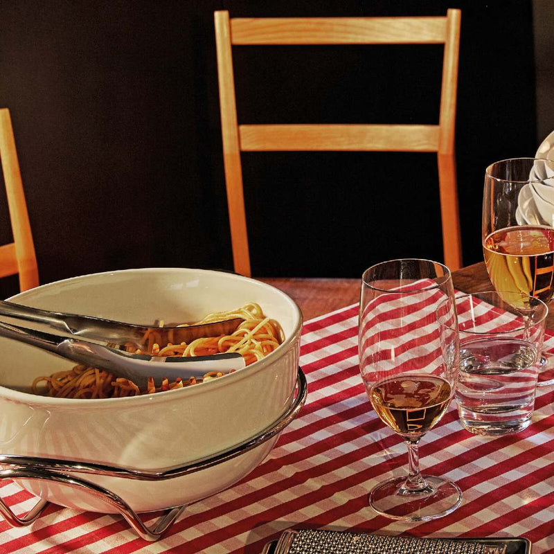 Dinner table with a bowl of pasta, wine glasses, and a glass of water on a red and white checkered tablecloth.