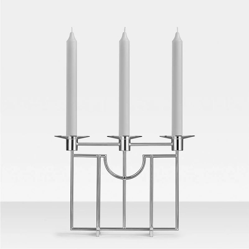 Silver candle holder with three white candles on a light gray background