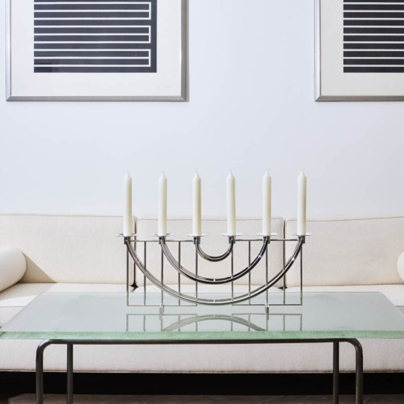 Decorative candle holder with candles on a glass coffee table in a living room setting.