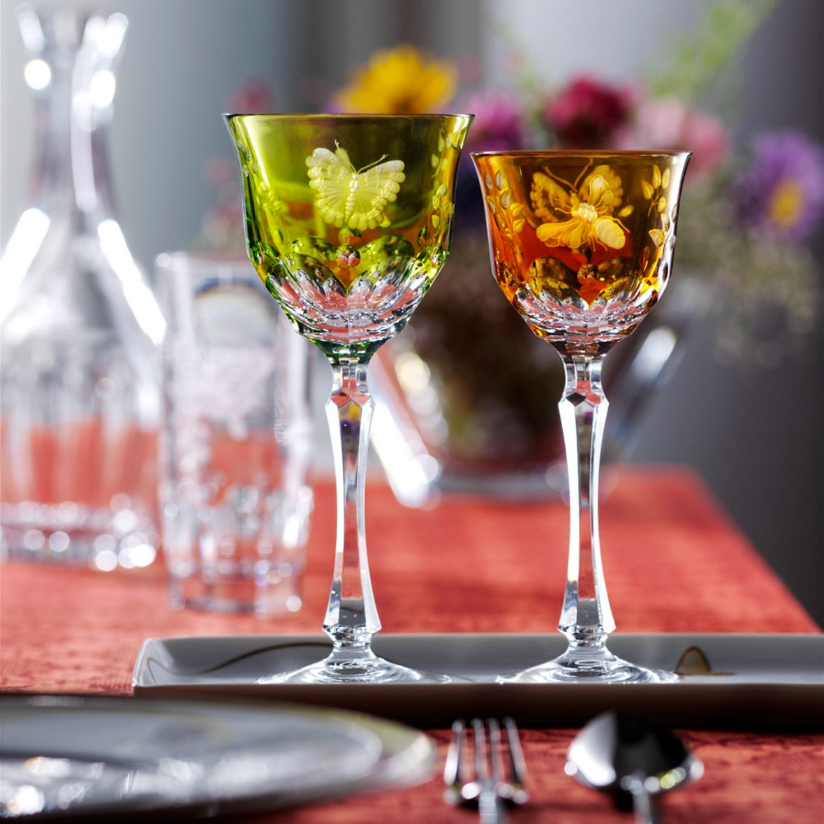 Two colorful glass goblets from the Springtime collection by Varga Crystal on a table with a blurred floral background
