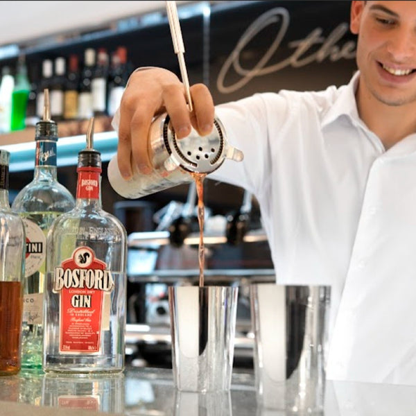 Barista pouring a drink from a cocktail shaker into a silver-plated spritz glass from Greggio Manhattan Collection with Bosford Gin bottles in the foreground.