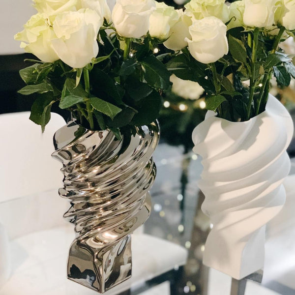 Two decorative vases with white flowers on a reflective surface