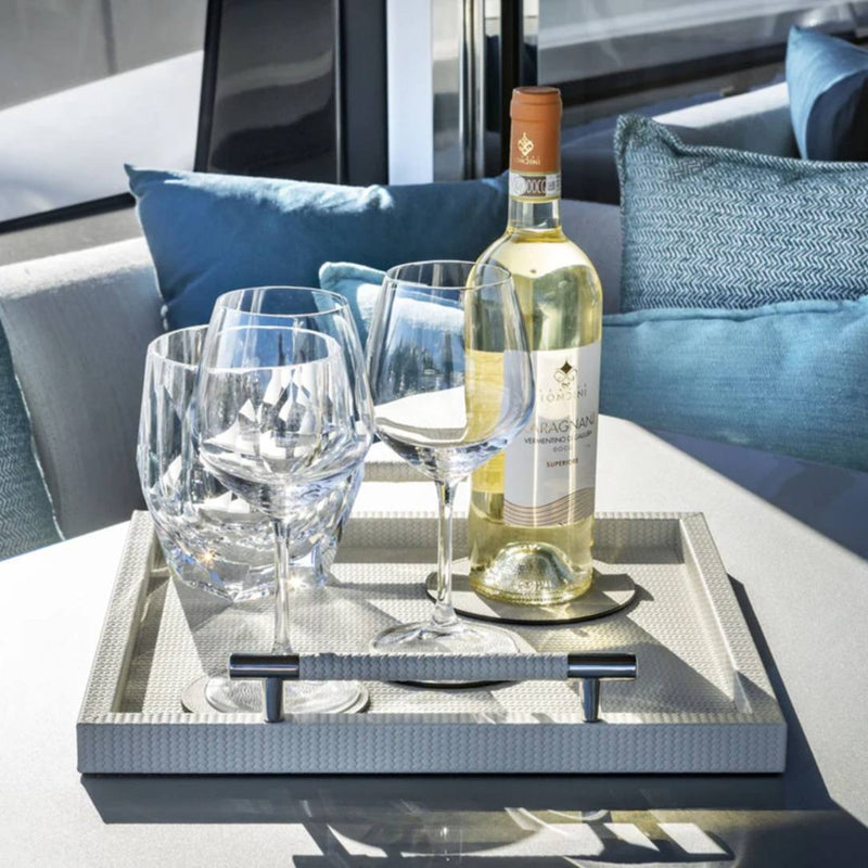 Wine bottle and glasses on a Square Woven Leather Tray with Handles Dedalo in Cream by Pinetti with a blurred outdoor background