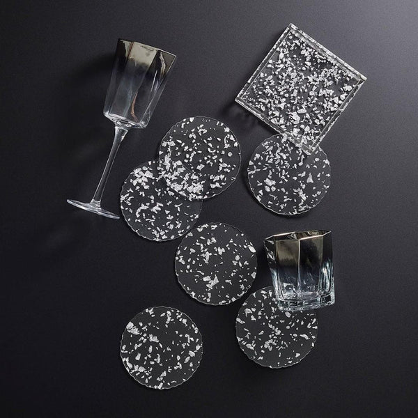 Set of clear and white speckled coasters with glasses on a dark surface