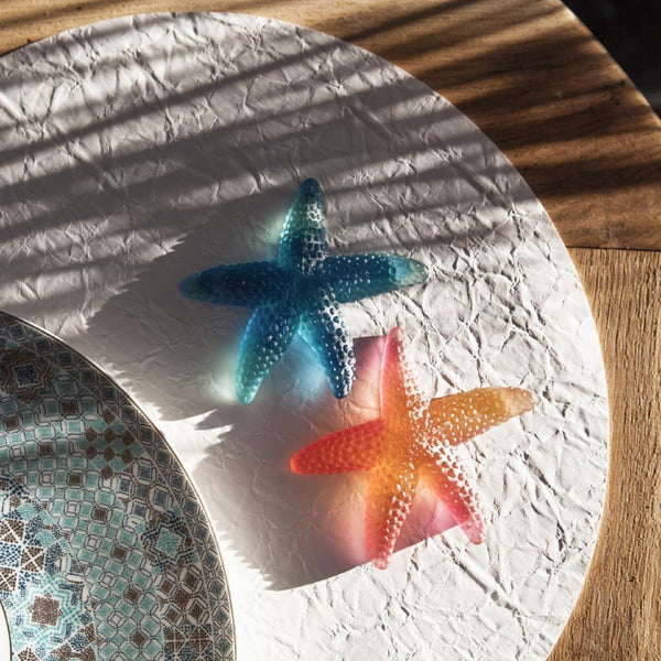 Two starfish-shaped objects one blue, one amber, on a textured surface with a wooden background