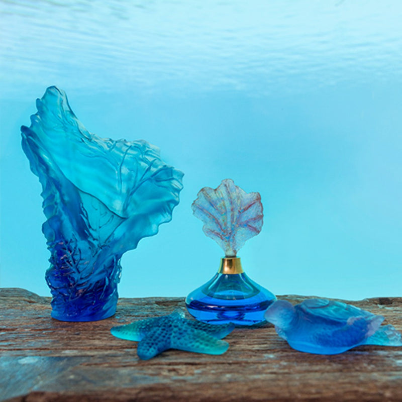 Blue shell-shaped perfume bottle on a wooden surface with a blue background