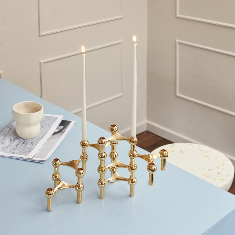 Gold candle holder with two lit candles on a light blue surface.