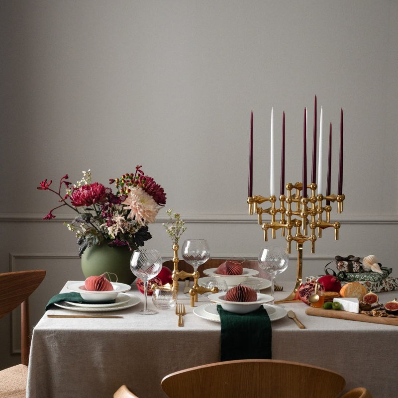 Elegant table setting with floral arrangement, candles, and cutlery on a neutral background