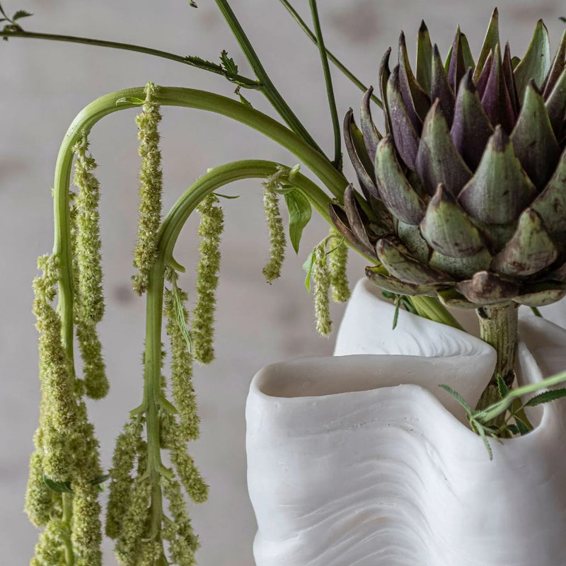 Artichoke with green leaves in a white vase against a neutral background